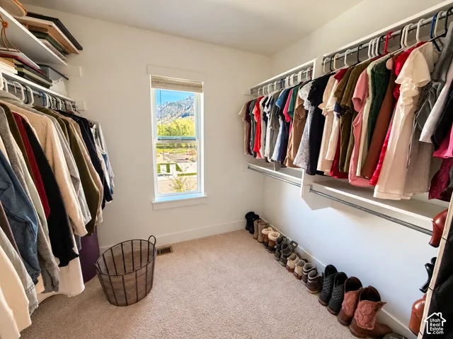 Walk-in closet featuring tiered built-in shelving, hanging rods, carpet flooring, and a window with mountain scenery