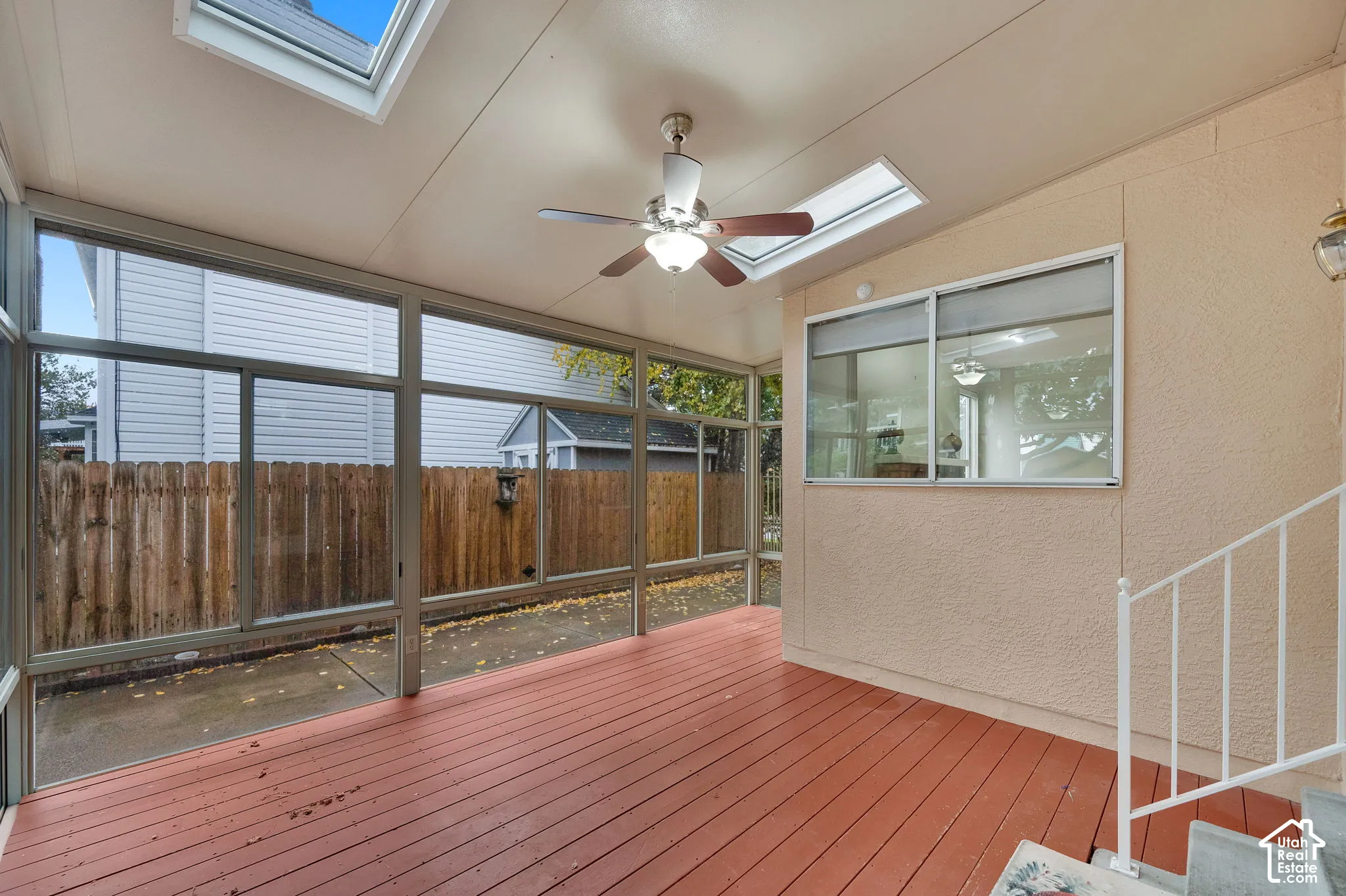 Enclosed sunroom featuring wood-finish decking, expansive glass windows, integrated skylights, and a ceiling fan with light fixture