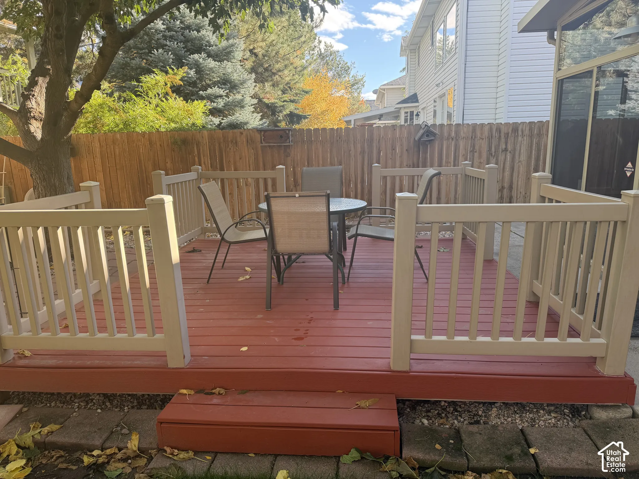 Raised exterior deck featuring composite wood-finish planking, neutral-tone vertical balustrades, a single-step entry, and surrounding wood privacy fencing