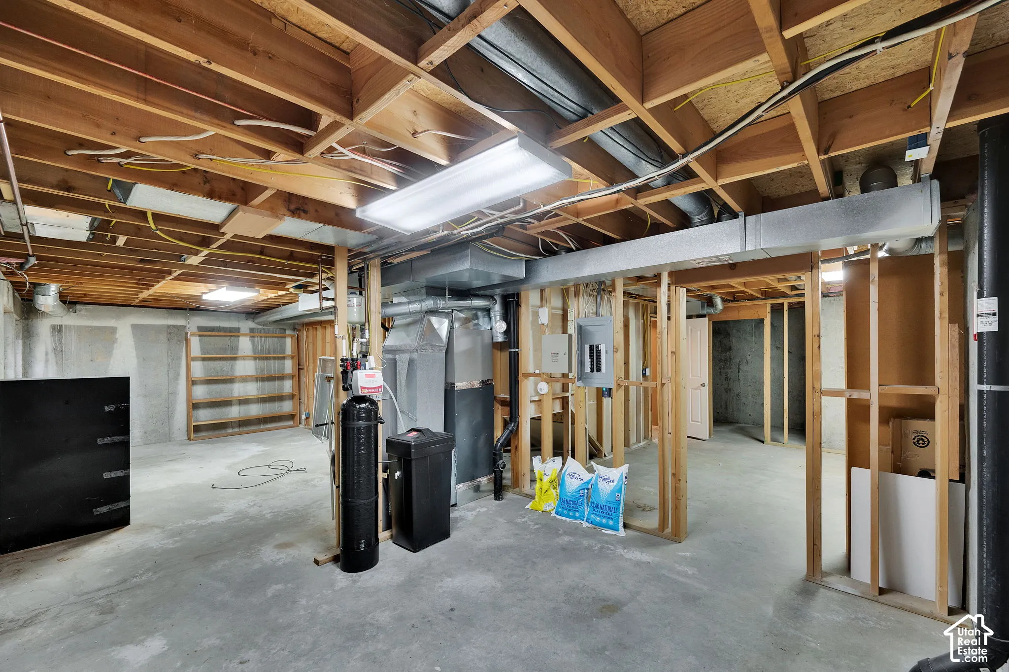 Unfinished lower level featuring exposed wood-joist ceiling, concrete flooring, structural wood framing, built-in shelving, and an integrated mechanical system