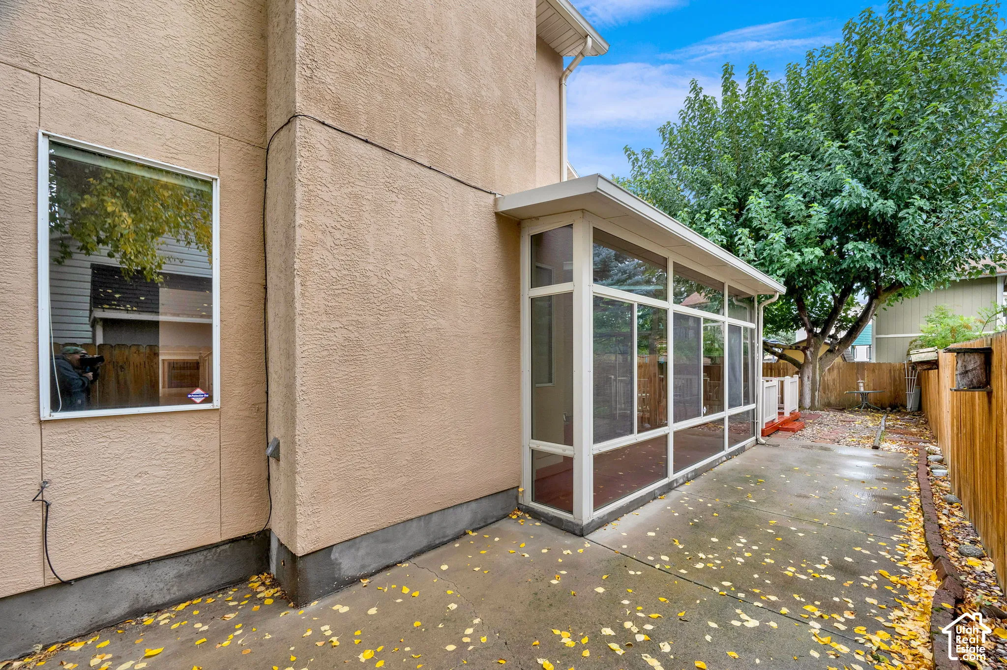 Stucco exterior featuring a screened-in enclosure, concrete patio, wood fencing, and mature trees