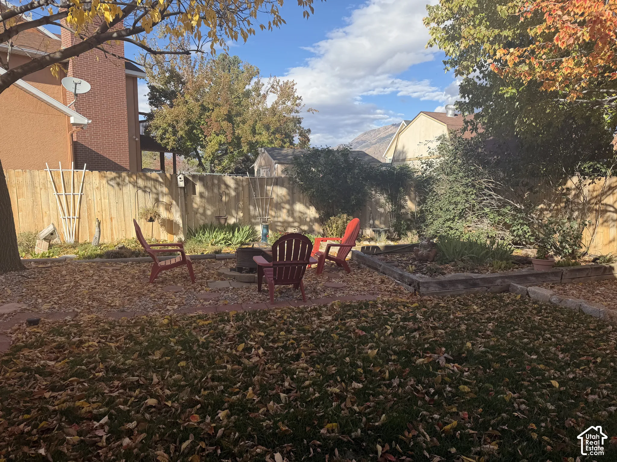 Backyard featuring wood-plank fencing, a circular stone fire pit, tiered timber garden beds, and mature trees with mountain backdrop