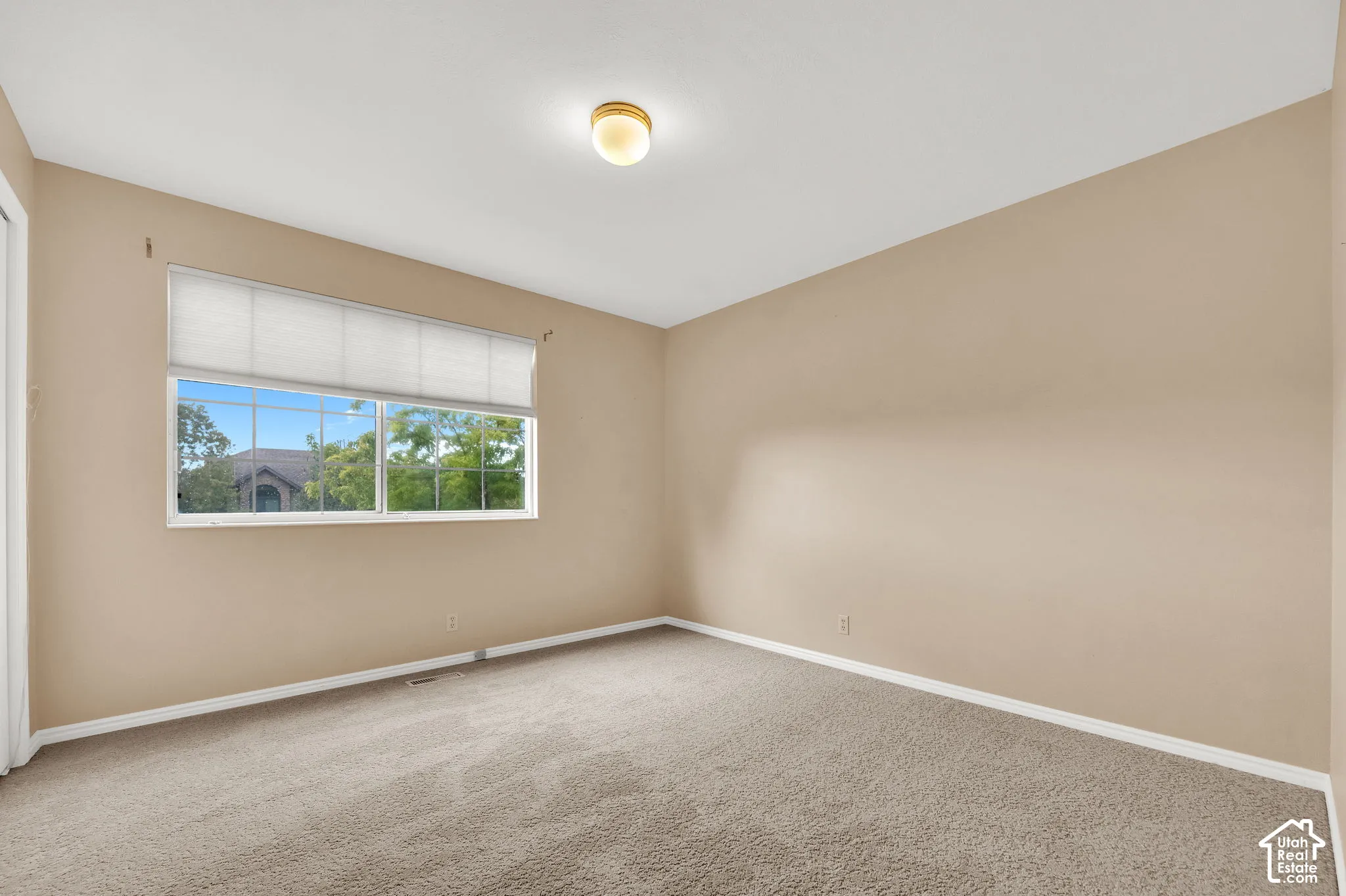 Neutral-toned interior space featuring neutral wall paint, carpeted flooring, a sliding window with integrated window treatment, and a flush-mount ceiling fixture