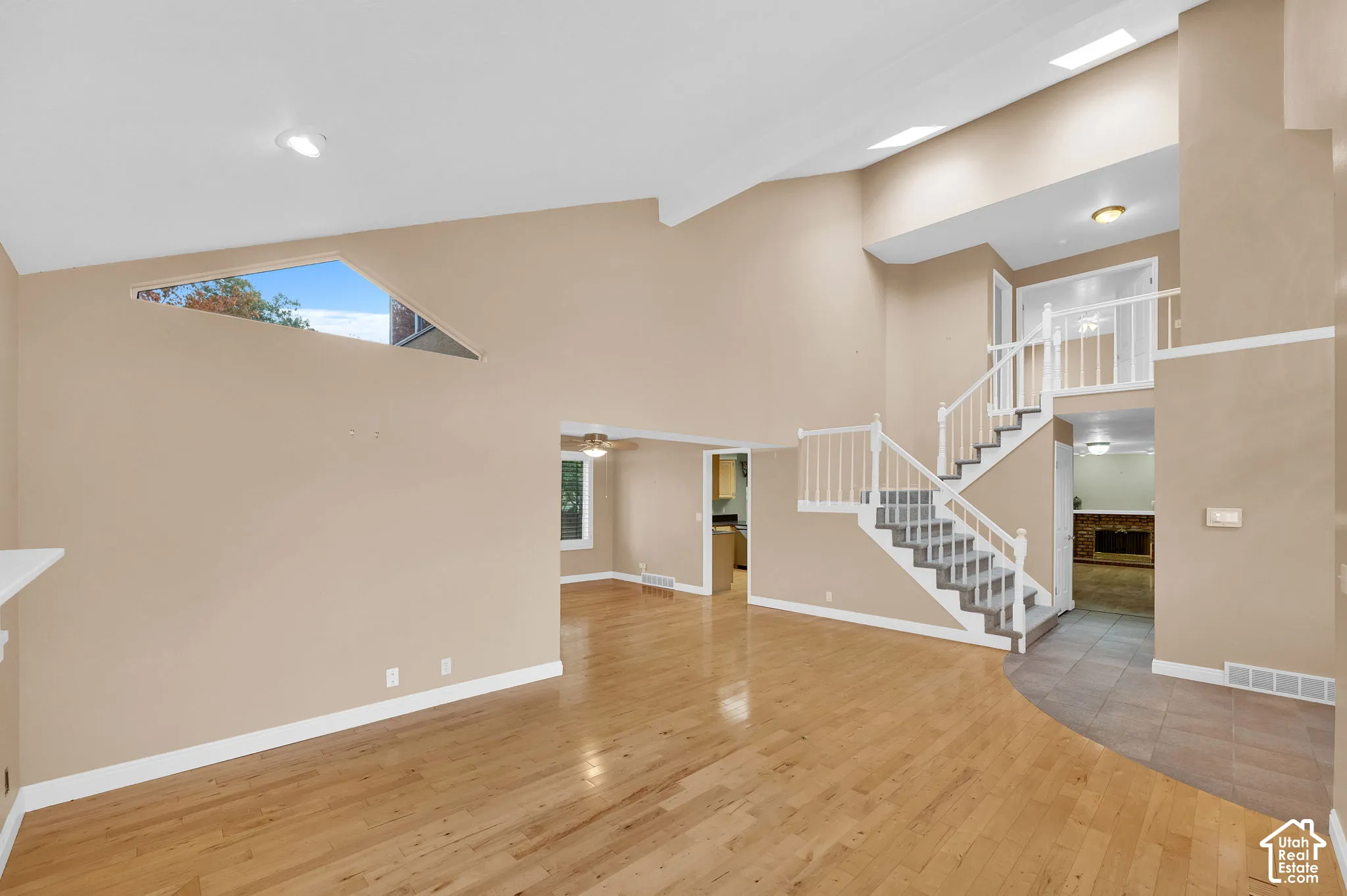 Vaulted ceiling with skylights, wood-finish flooring, staircase with white spindle railing, and geometric accent window