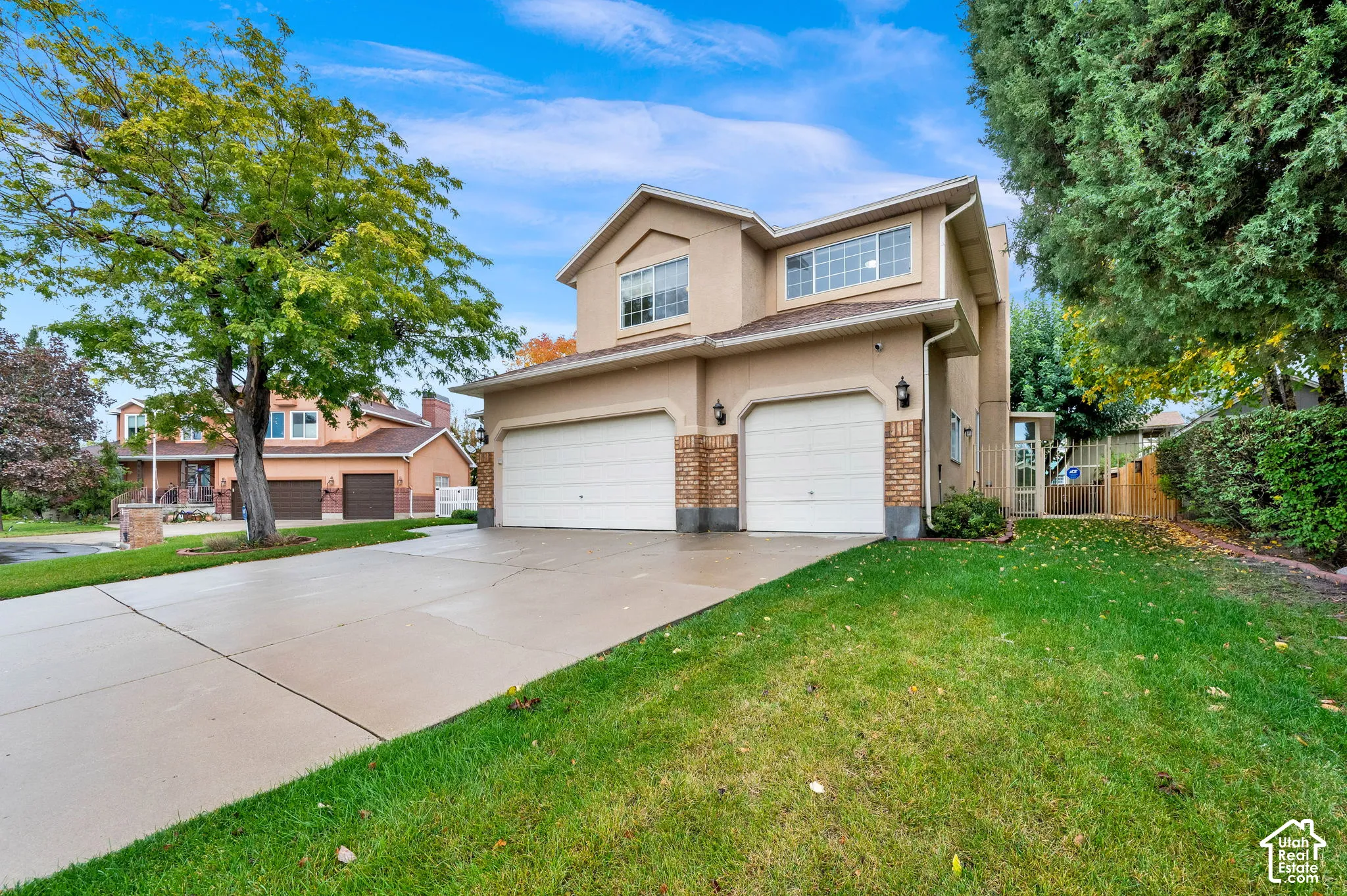 Two-story stucco exterior featuring a two-car garage, brick accents, concrete driveway, and mature landscaping