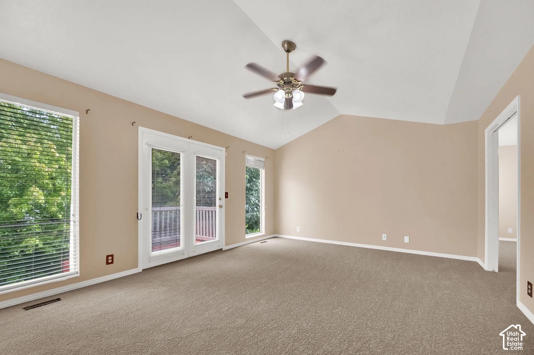 Vaulted ceilings, neutral carpeting, a dual-blade ceiling fan with light fixture, and glass-paned double doors with integrated blinds