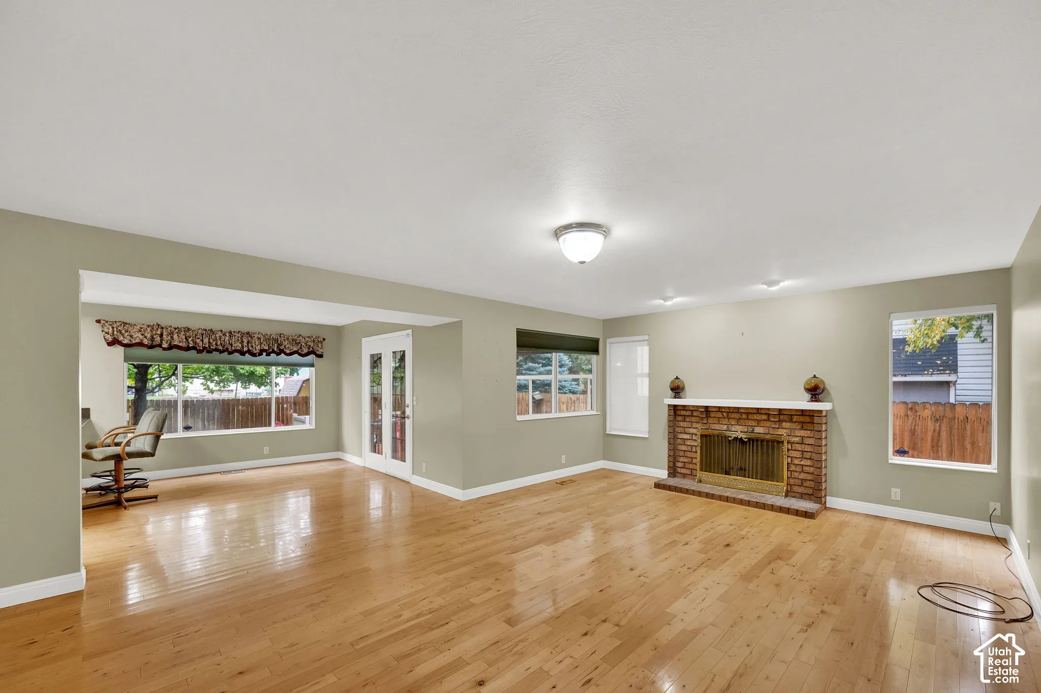 Living area featuring wood-finish flooring, a floor-to-ceiling brick fireplace with a mantle, double glass-panel doors, and large windows providing natural light