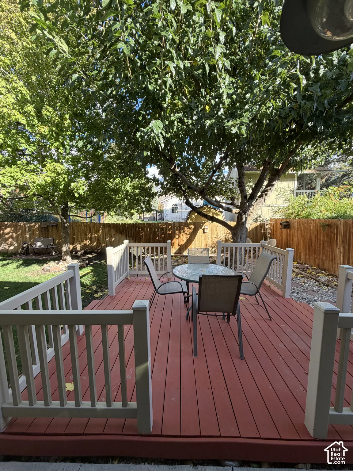 Raised wooden deck featuring light-colored railings, privacy fencing, and mature canopy trees