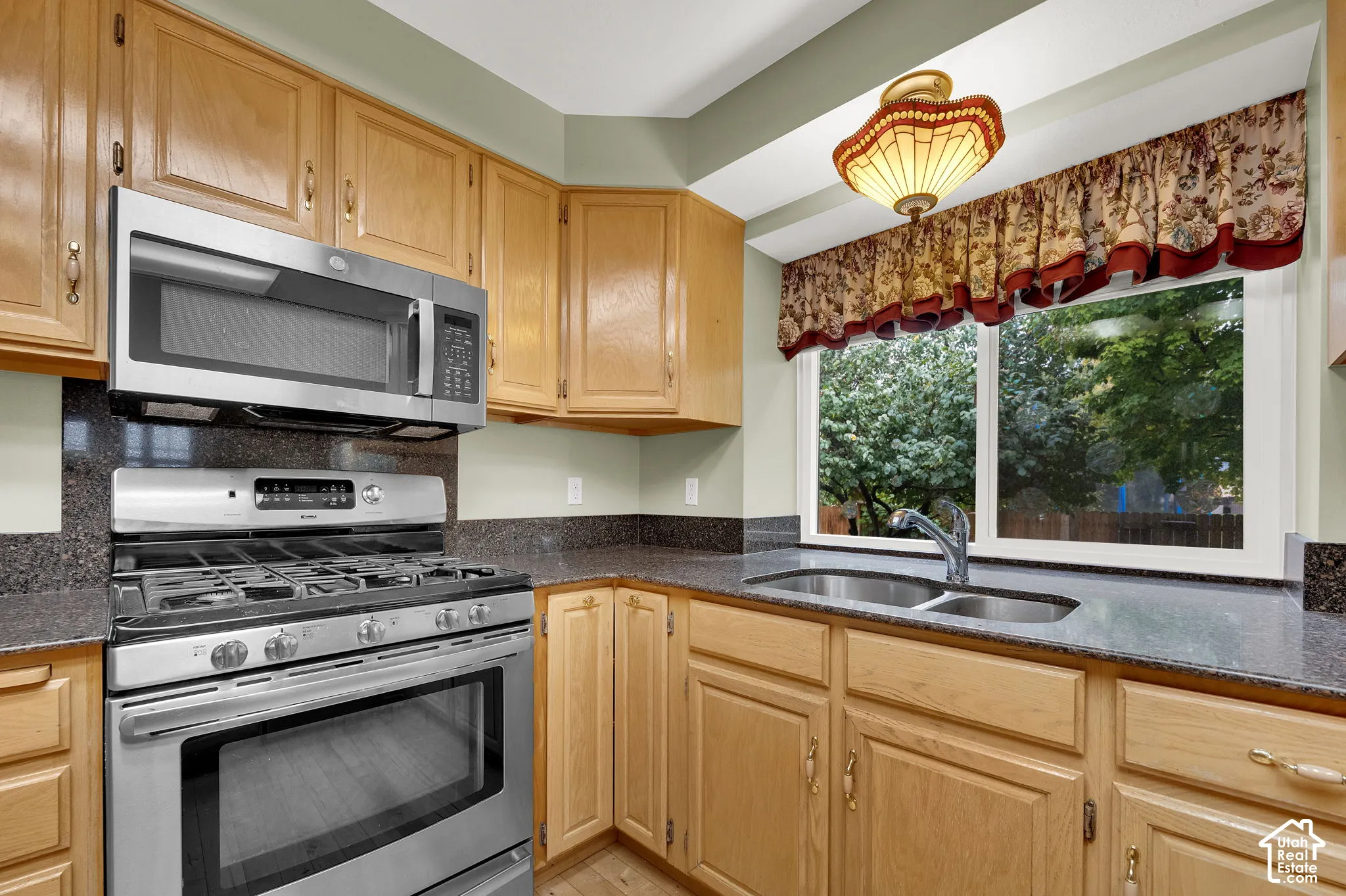 Kitchen featuring natural wood cabinetry, stone-finish countertops, stainless steel gas range, over-the-range microwave, and stainless steel dual-basin undermount sink