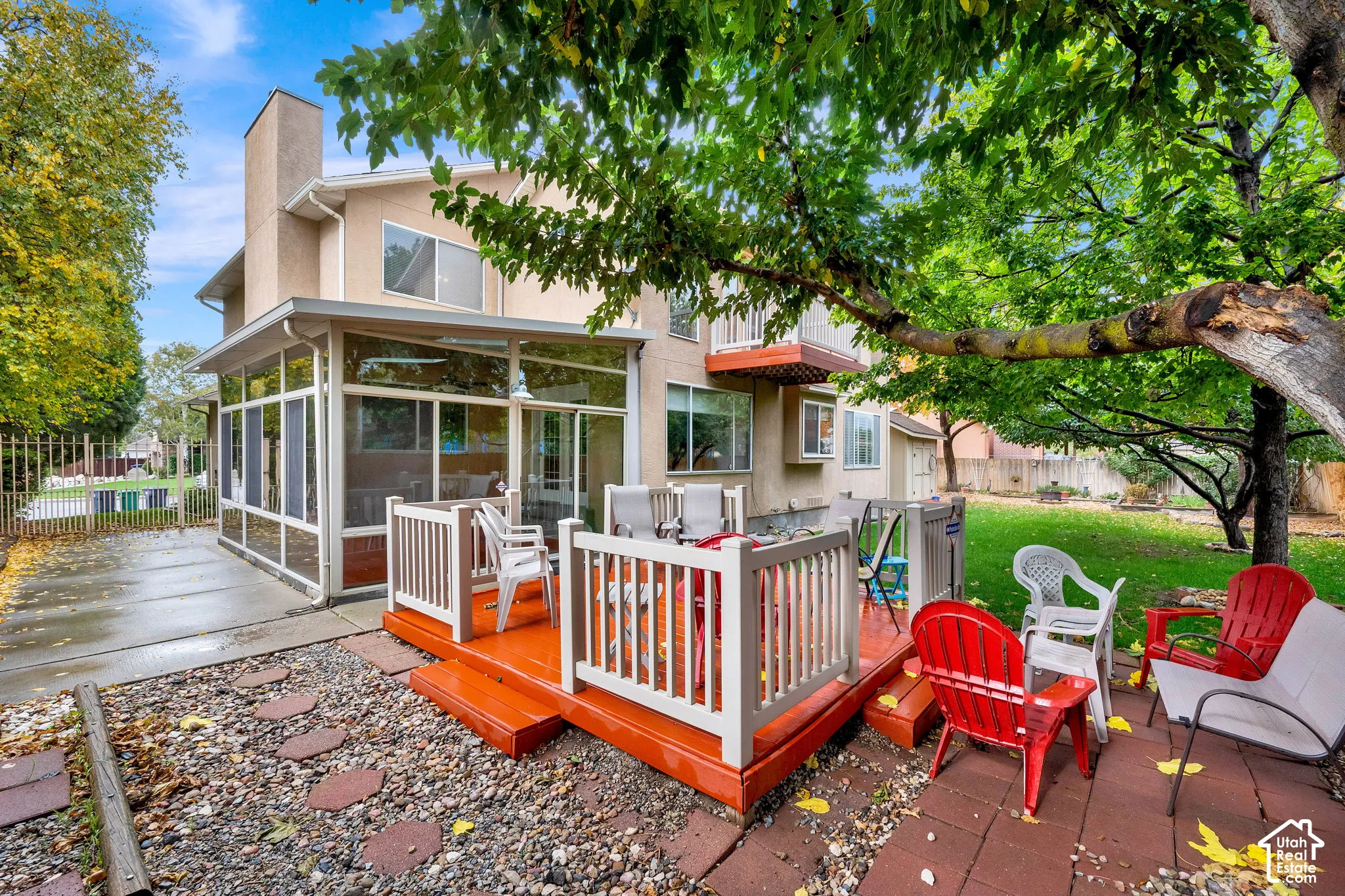 Multi-story exterior featuring a screened-in porch, raised wood-finish deck with railing, concrete patio area, and mature trees