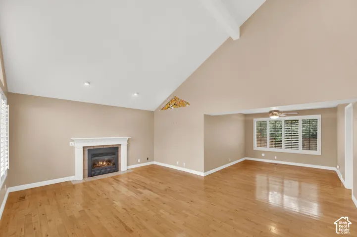 Vaulted ceiling, wood-finish flooring, white fireplace mantel, recessed lighting, and multi-pane window with plantation shutters