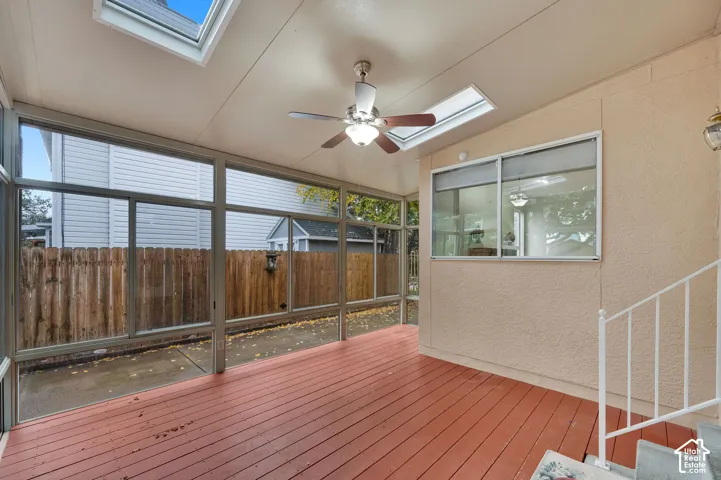 Enclosed sunroom featuring wood-finish decking, expansive glass windows, integrated skylights, and a ceiling fan with light fixture