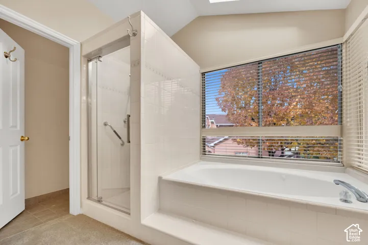 Bathroom featuring a deep-basin soaking tub with tiled surround, a separate glass-enclosed shower, and a vaulted ceiling