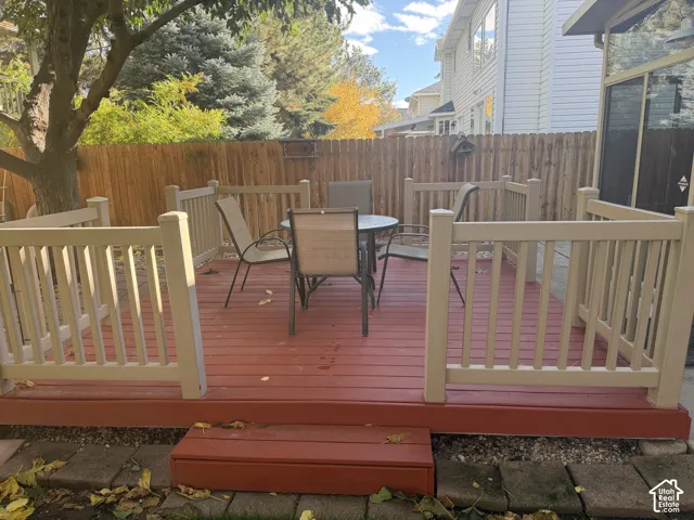 Raised exterior deck featuring composite wood-finish planking, neutral-tone vertical balustrades, a single-step entry, and surrounding wood privacy fencing