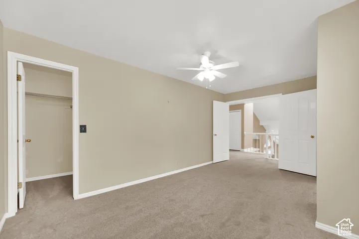 Room featuring neutral carpeting, a ceiling fan with integrated lighting, a walk-in closet, and white interior doors