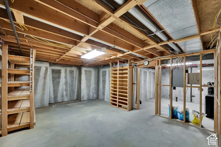 Unfinished lower level featuring exposed wood-joist ceiling, concrete foundation walls, concrete flooring, and built-in wood shelving units