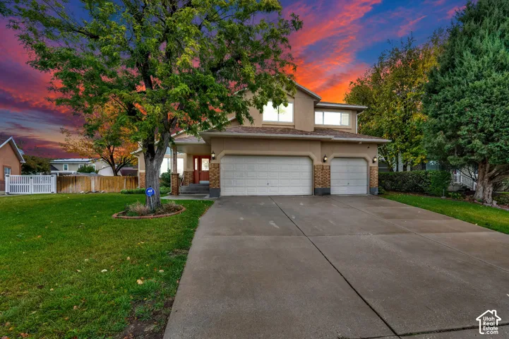 Stucco exterior featuring a three-car garage, concrete driveway, mature landscaping, and an expansive front lawn