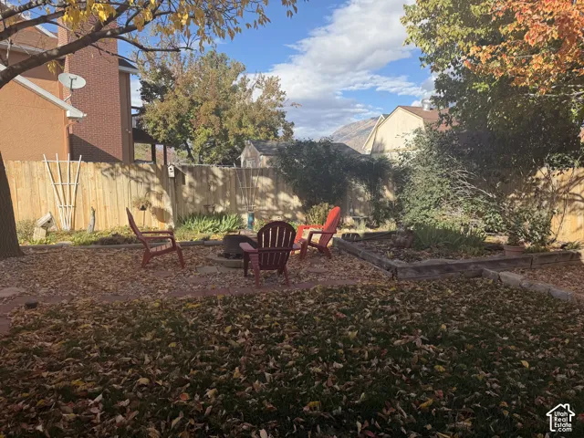 Backyard featuring wood-plank fencing, a circular stone fire pit, tiered timber garden beds, and mature trees with mountain backdrop