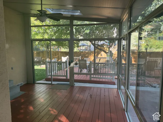 Enclosed patio featuring wood-finish flooring, a ceiling fan, a skylight, and large sliding glass panels
