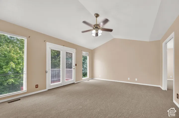 Vaulted ceilings, neutral carpeting, a dual-blade ceiling fan with light fixture, and glass-paned double doors with integrated blinds