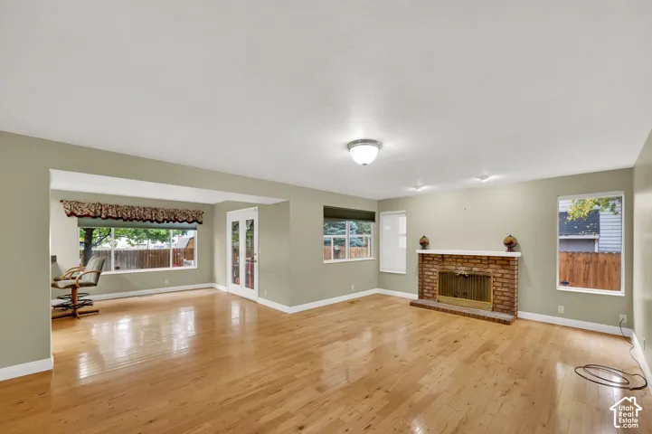 Living area featuring wood-finish flooring, a floor-to-ceiling brick fireplace with a mantle, double glass-panel doors, and large windows providing natural light
