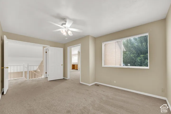 Carpeted interior room featuring a multi-light ceiling fan and a large horizontal sliding window with interior blinds