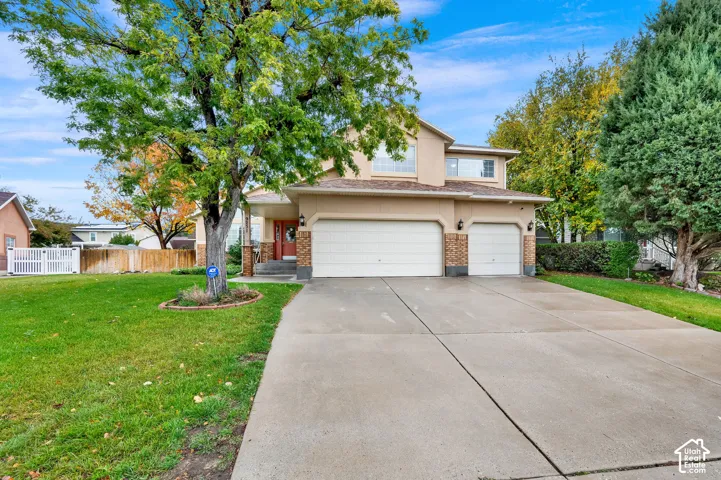 Two-story stucco exterior featuring stone veneer accents, a three-car garage, concrete driveway, and established landscaping