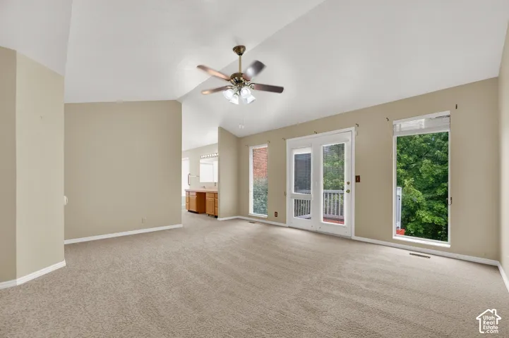 Vaulted ceilings featuring a central overhead fan, dual vertical windows, and glass-paneled exterior door