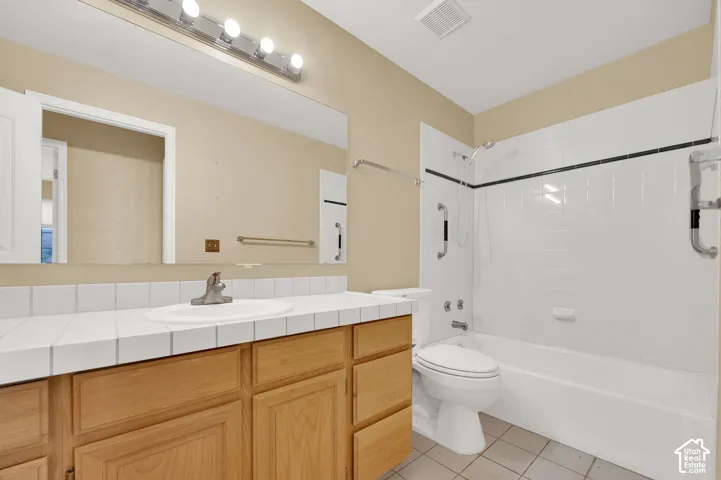Bathroom featuring a vanity with a white tiled countertop, integrated basin, natural-finish wood cabinetry, a large wall-mounted mirror, and a tub-shower combination with white wall tile