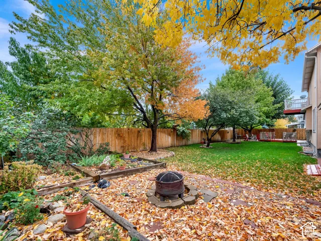 Backyard featuring a stone-bordered patio, fire pit, timber-edged landscaping beds, mature trees, and wood privacy fencing