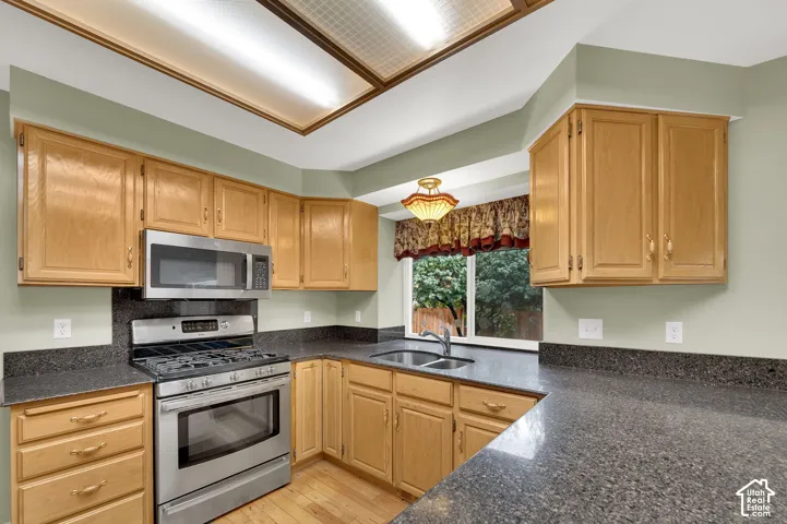 Kitchen featuring natural wood cabinetry, dark stone countertops, stainless steel gas range, built-in microwave, and wood-finish flooring