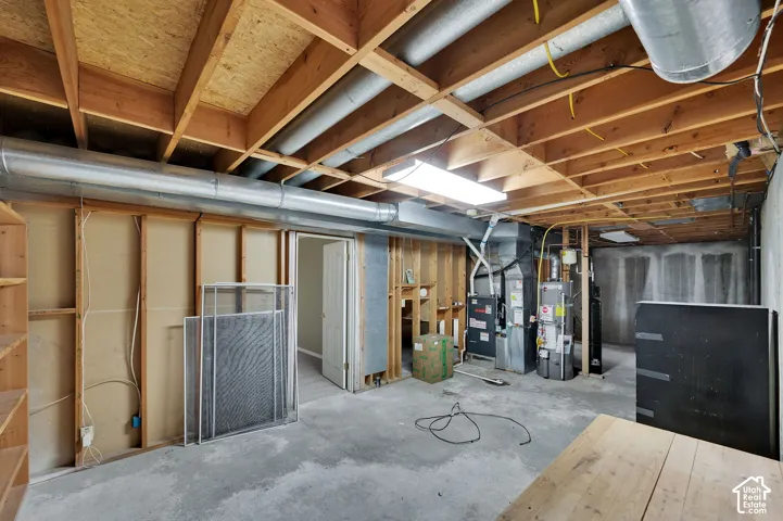 Utility space with an exposed wood-joist ceiling, concrete flooring, furnace, and water heater