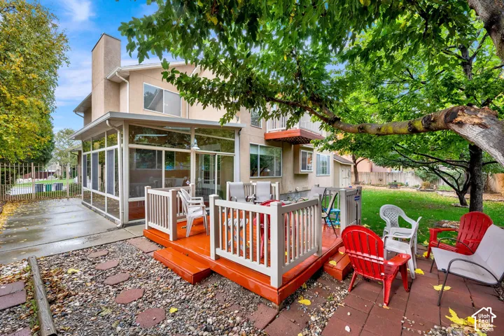 Multi-story exterior featuring a screened-in porch, raised wood-finish deck with railing, concrete patio area, and mature trees