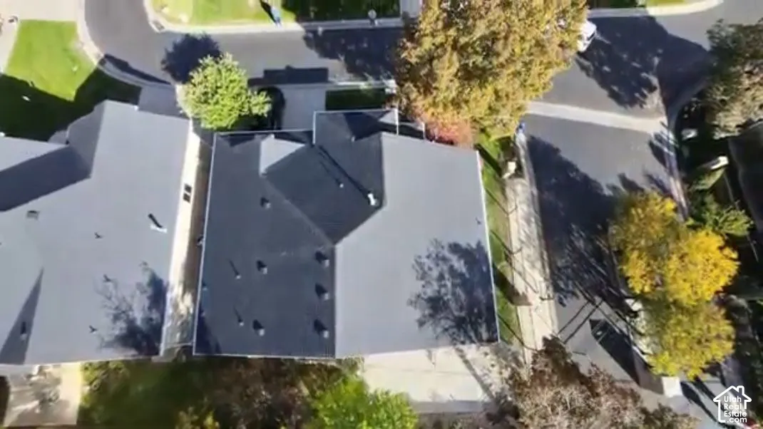 Aerial perspective of a multi-faceted shingle roof, concrete driveway, and mature landscaping