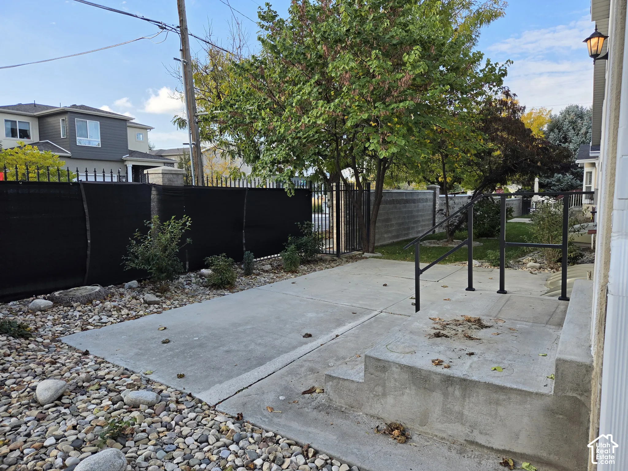 Concrete patio featuring stone landscaping, metal perimeter fencing, and concrete steps with black metal handrails