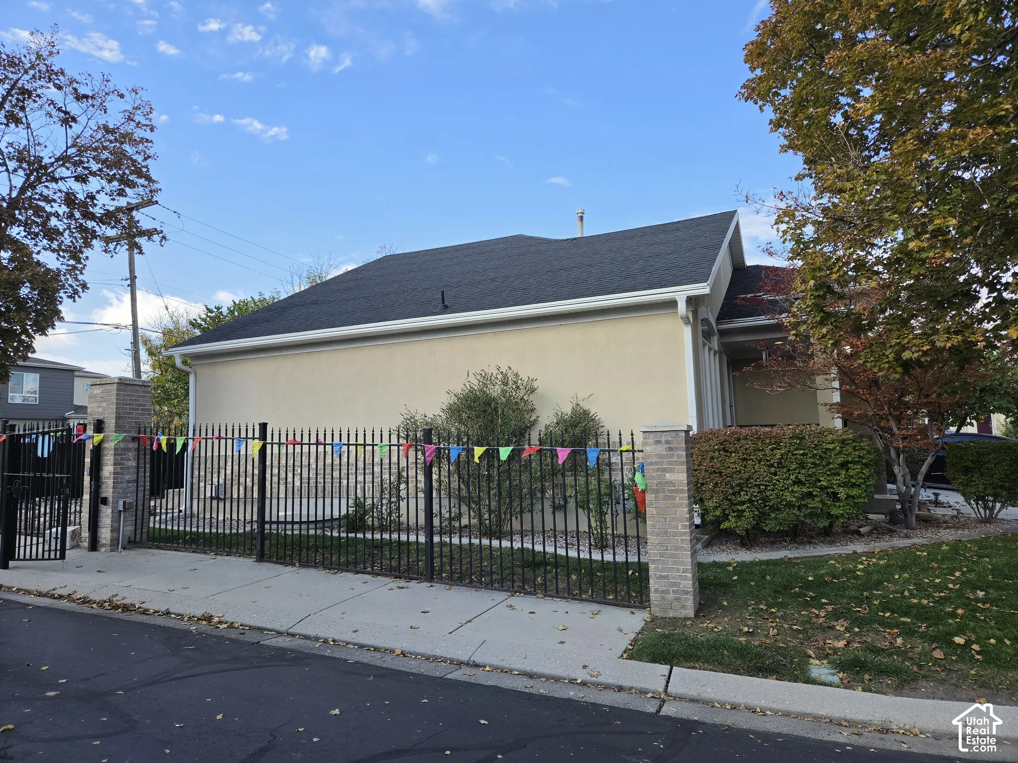 Stucco exterior with stone veneer accents, dark asphalt shingle roof, and full-perimeter metal fencing with stone-capped masonry pillars