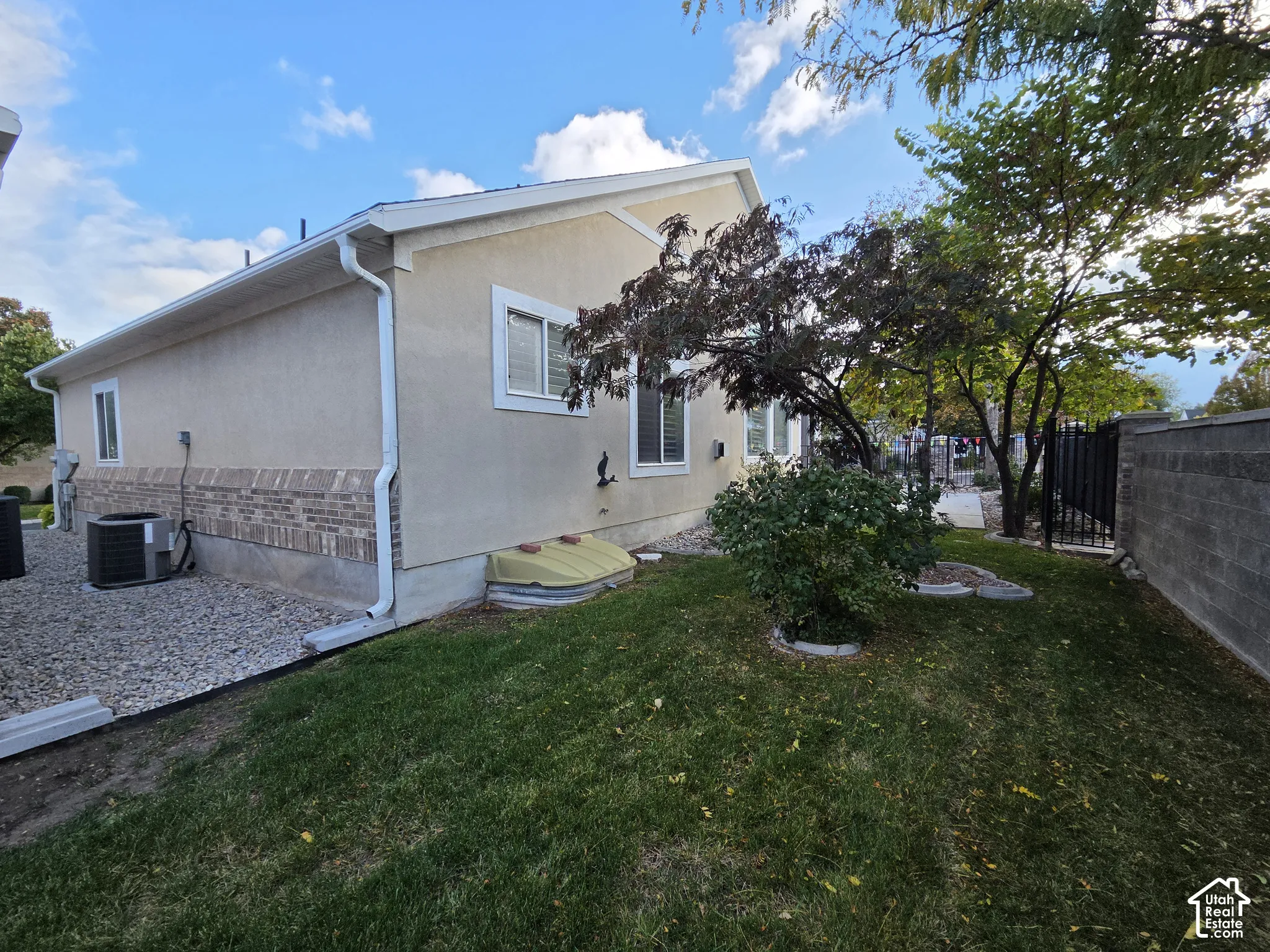 Exterior side yard featuring stucco and brick veneer siding, a lawn area, mature trees, and a decorative block wall