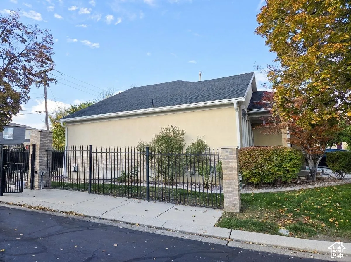 Stucco exterior with stone veneer accents, dark shingle roof, and full-height metal fencing with integrated stone masonry pillars