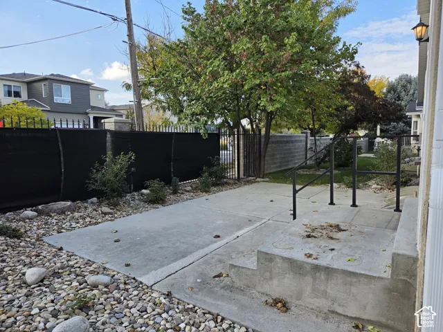 Concrete patio featuring stone landscaping, metal perimeter fencing, and concrete steps with black metal handrails