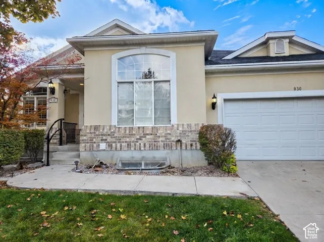 Stucco exterior featuring brick wainscoting, arched picture window, concrete driveway, and covered entryway