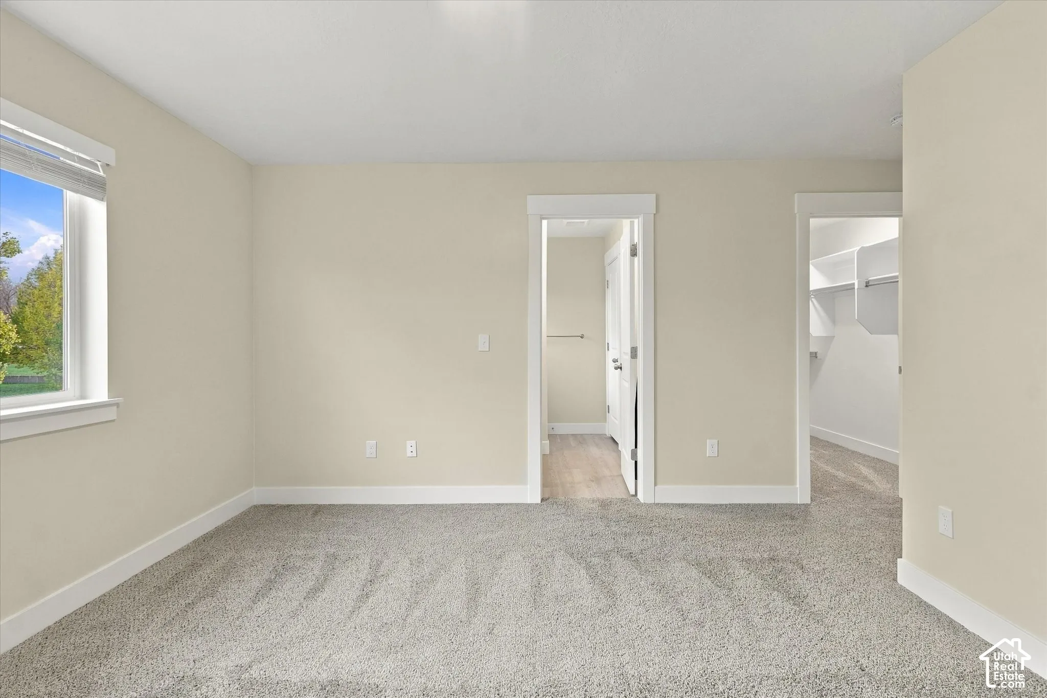 Primary bedroom featuring wall-to-wall carpeting, window with trim surround, and two interior entryways leading to primary bathroom and walk-in closet