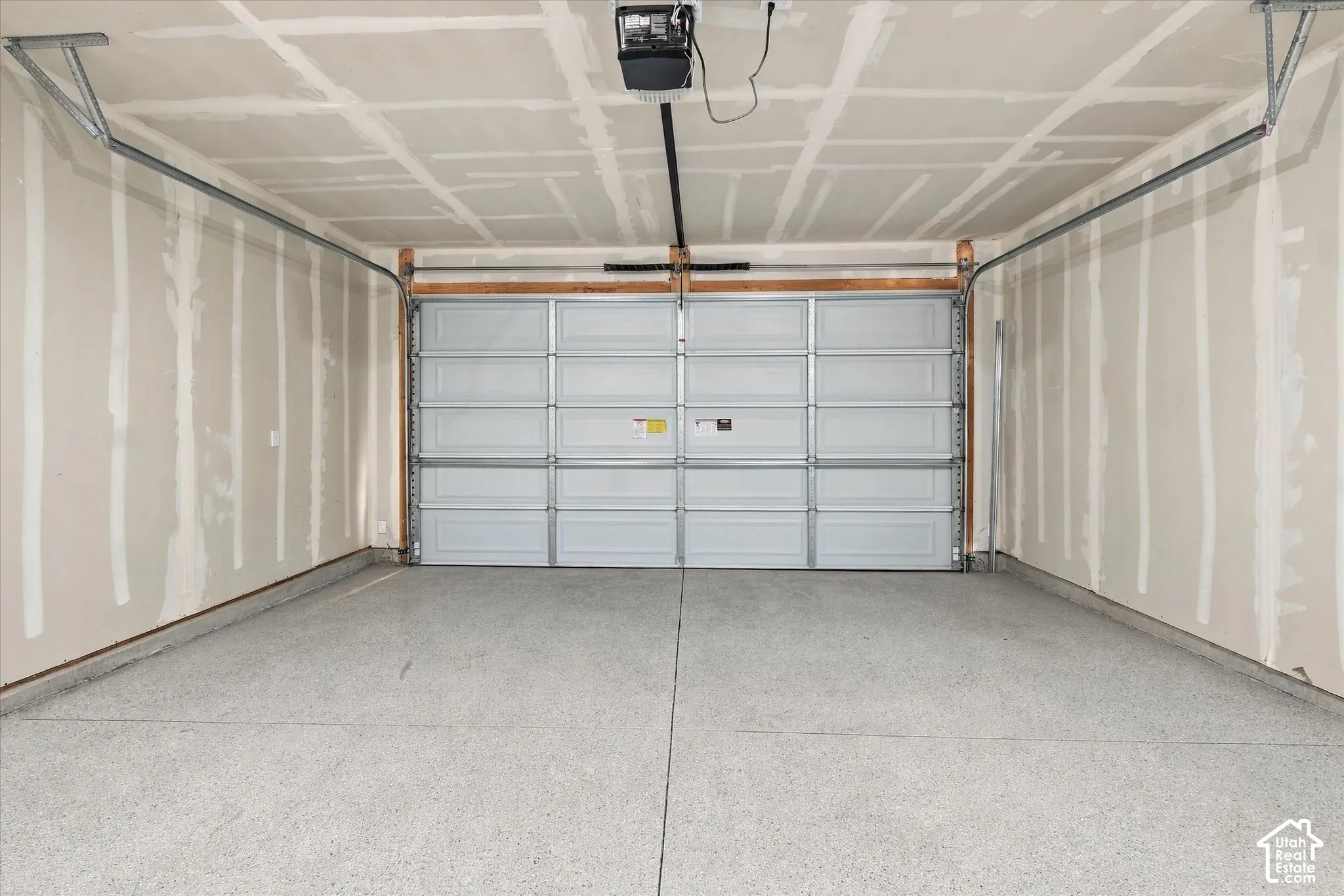 Two-car garage featuring a segmented overhead door, durable speckled epoxy flooring, and an automated door opener mechanism