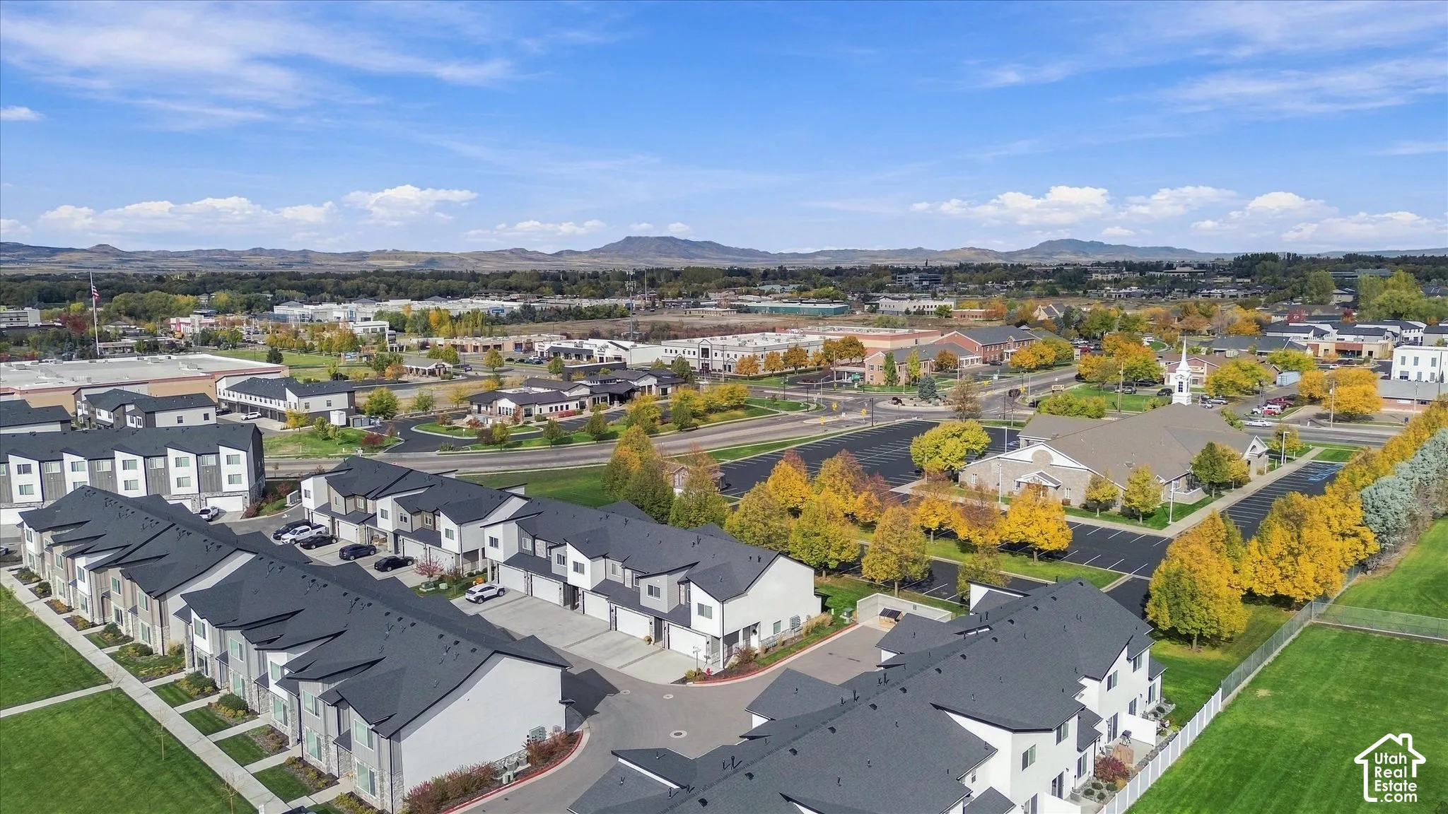Aerial perspective of multi-family structures featuring dark shingled roofs, concrete driveways, and expansive grassy lawn areas set against a mountain backdrop