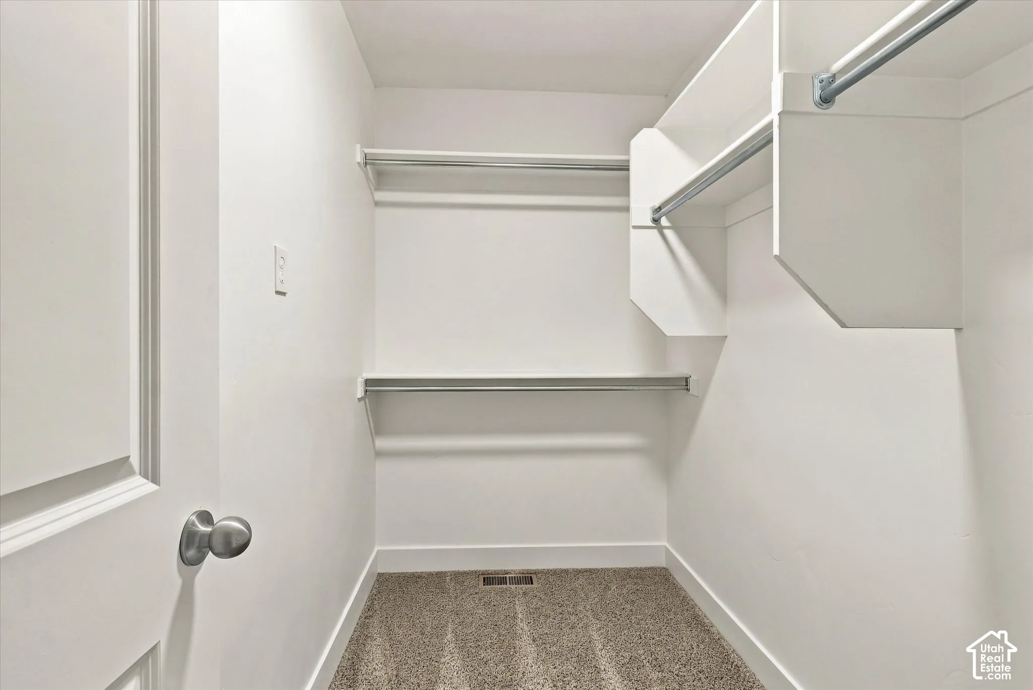 Walk-in closet featuring multi-level white built-in shelving, integrated metal clothing rods, and wall-to-wall carpeting
