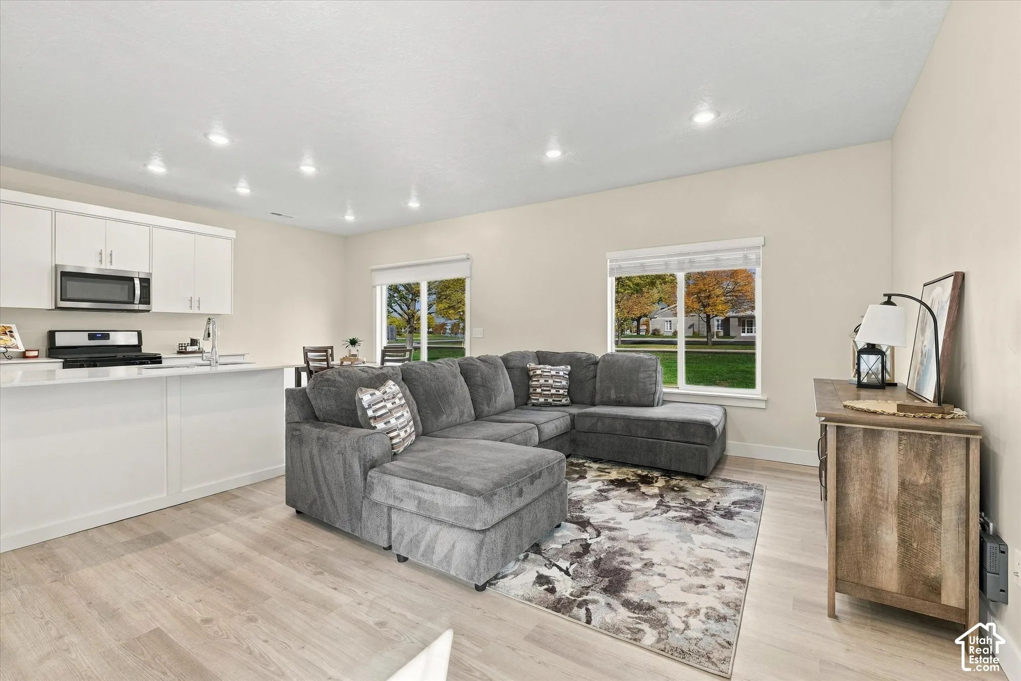 Open-concept kitchen featuring white cabinetry, a built-in microwave, and recessed ceiling lighting, complemented by wood-finish flooring and large windows