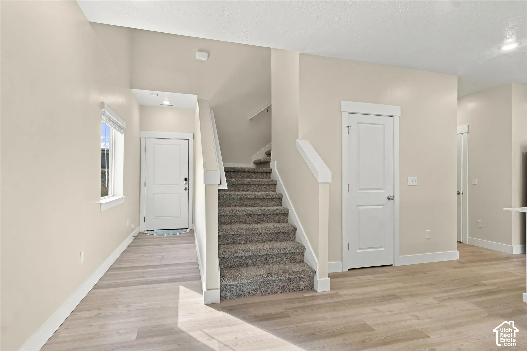Entryway featuring wood-finish flooring, vaulted ceilings, carpeted staircase with white handrails, and multi-panel interior doors