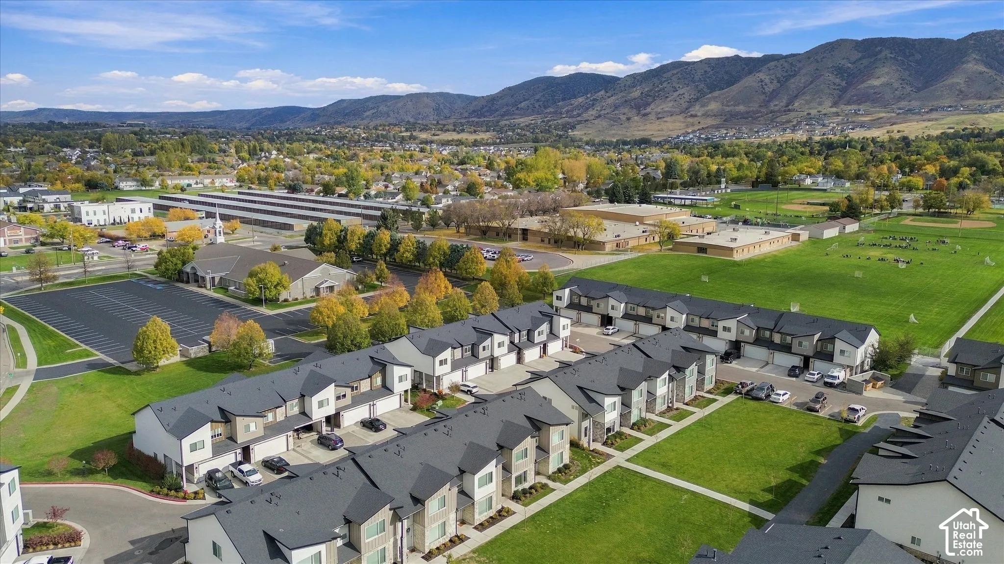 Aerial view of multi-unit residential complex featuring asphalt shingle roofing, attached garages, stone and siding exterior finishes, and shared green space