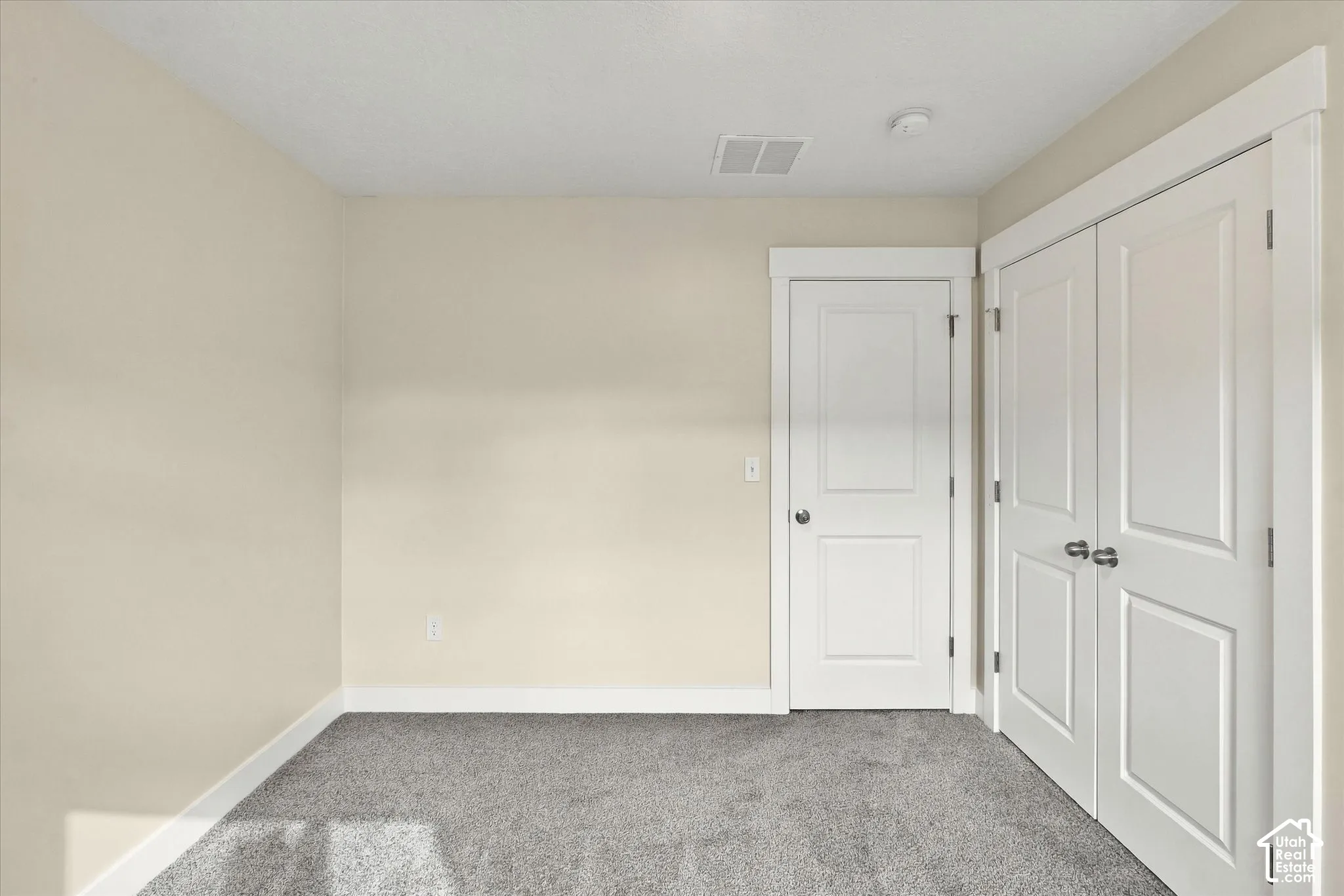 Bedroom with plush wall-to-wall carpeting, white paneled interior door, and double-door closet with brushed nickel hardware