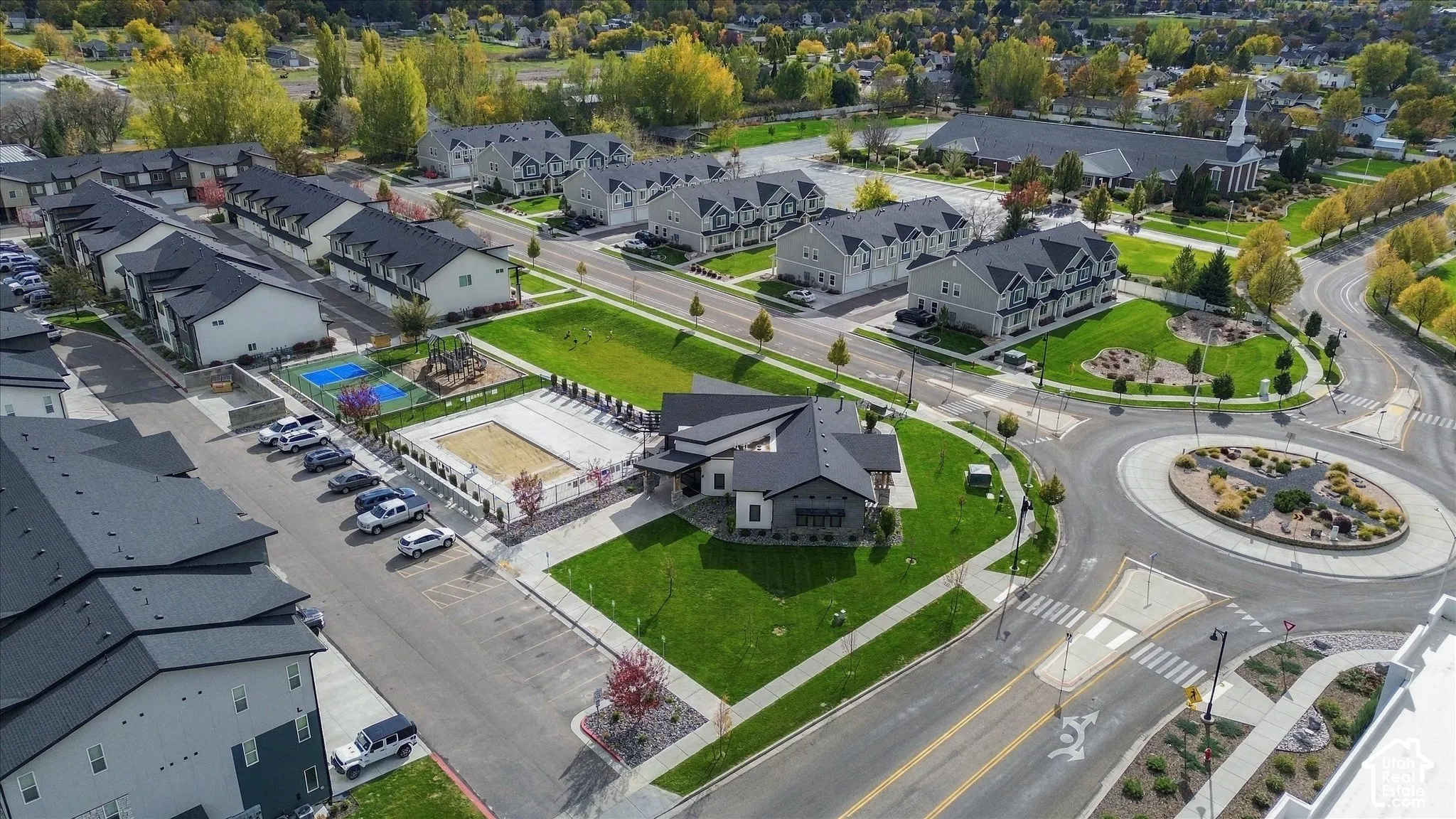 Aerial perspective featuring a multi-unit residential community with a swimming pool, fenced sport court, designated surface parking, and landscaped green spaces