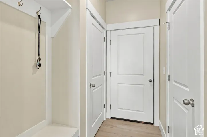 Mudroom featuring built-in wall-mounted coat hooks, an integrated shelf, wood-finish flooring, and white two-panel doors with satin nickel hardware